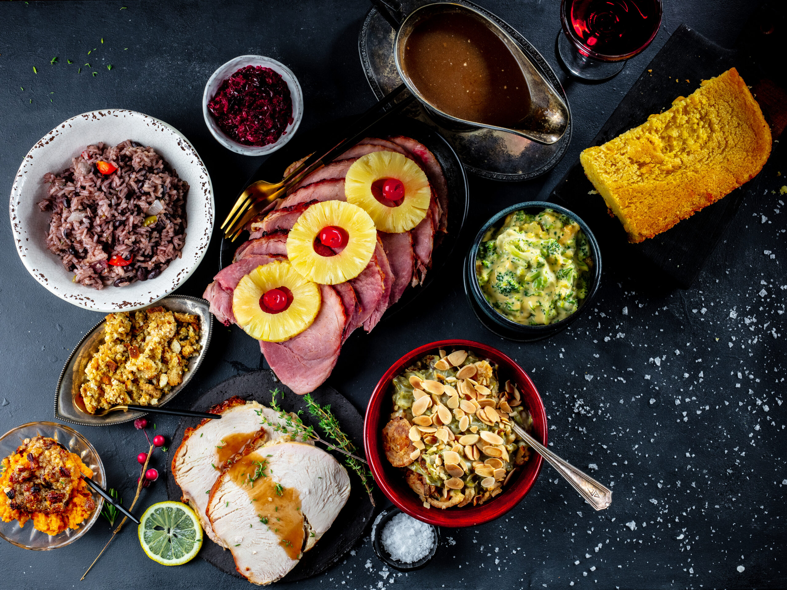 A spread of ham, turkey, gravy, green bean casserole on a dark table