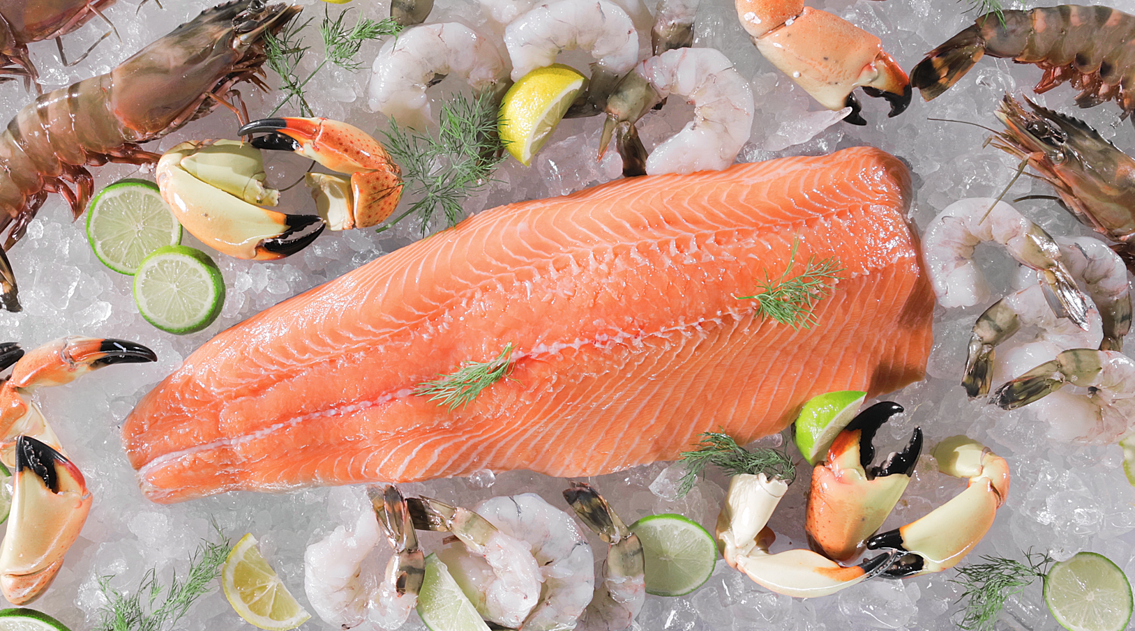A large raw Faroe Islands salmon fillet on ice, surrounded by shrimp, crab claws, lobster, and lime slices. Sprigs of dill garnish the salmon.